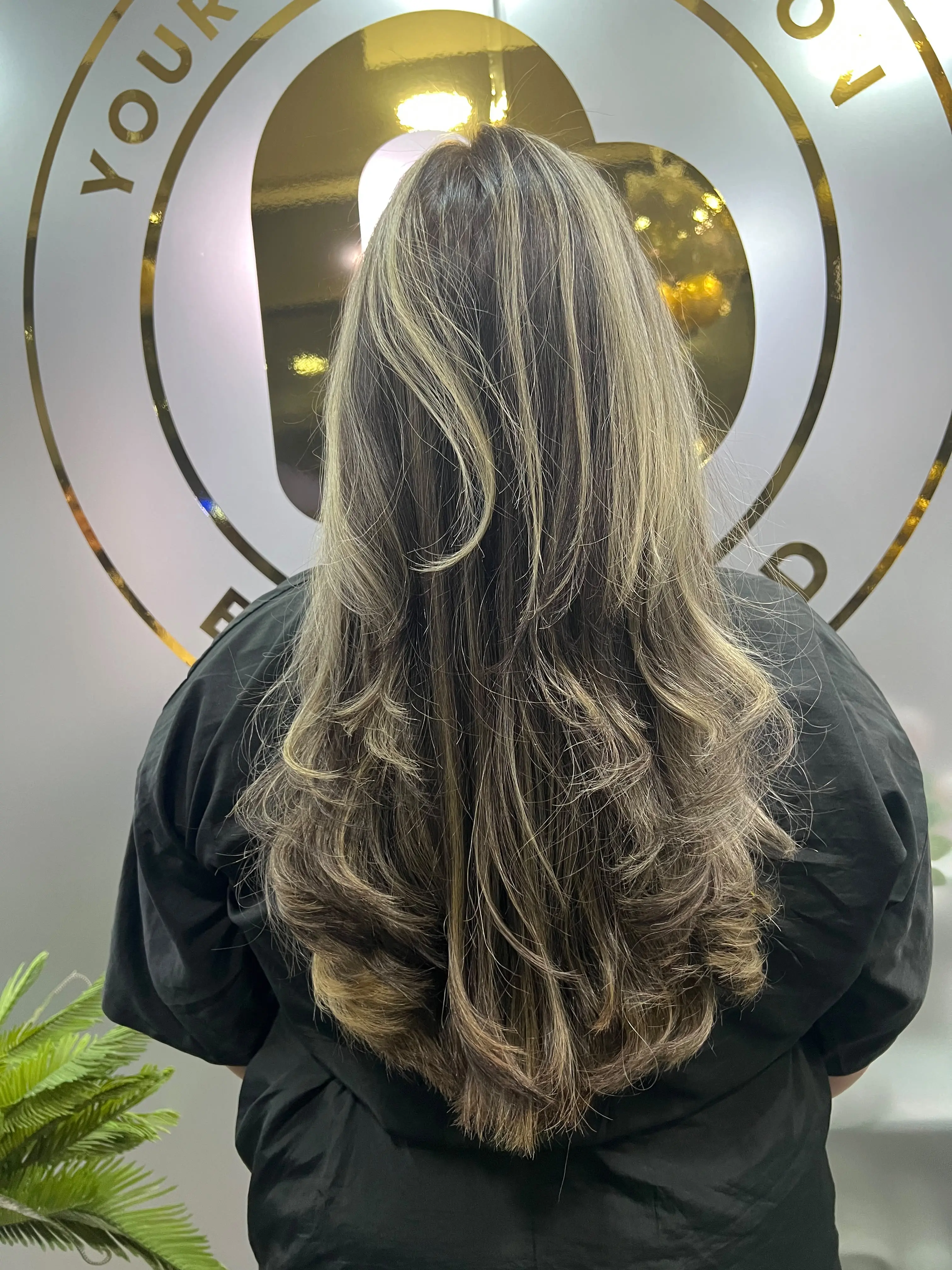 Cabello largo con raíz castaña y transición a luces rubias, visto desde atrás